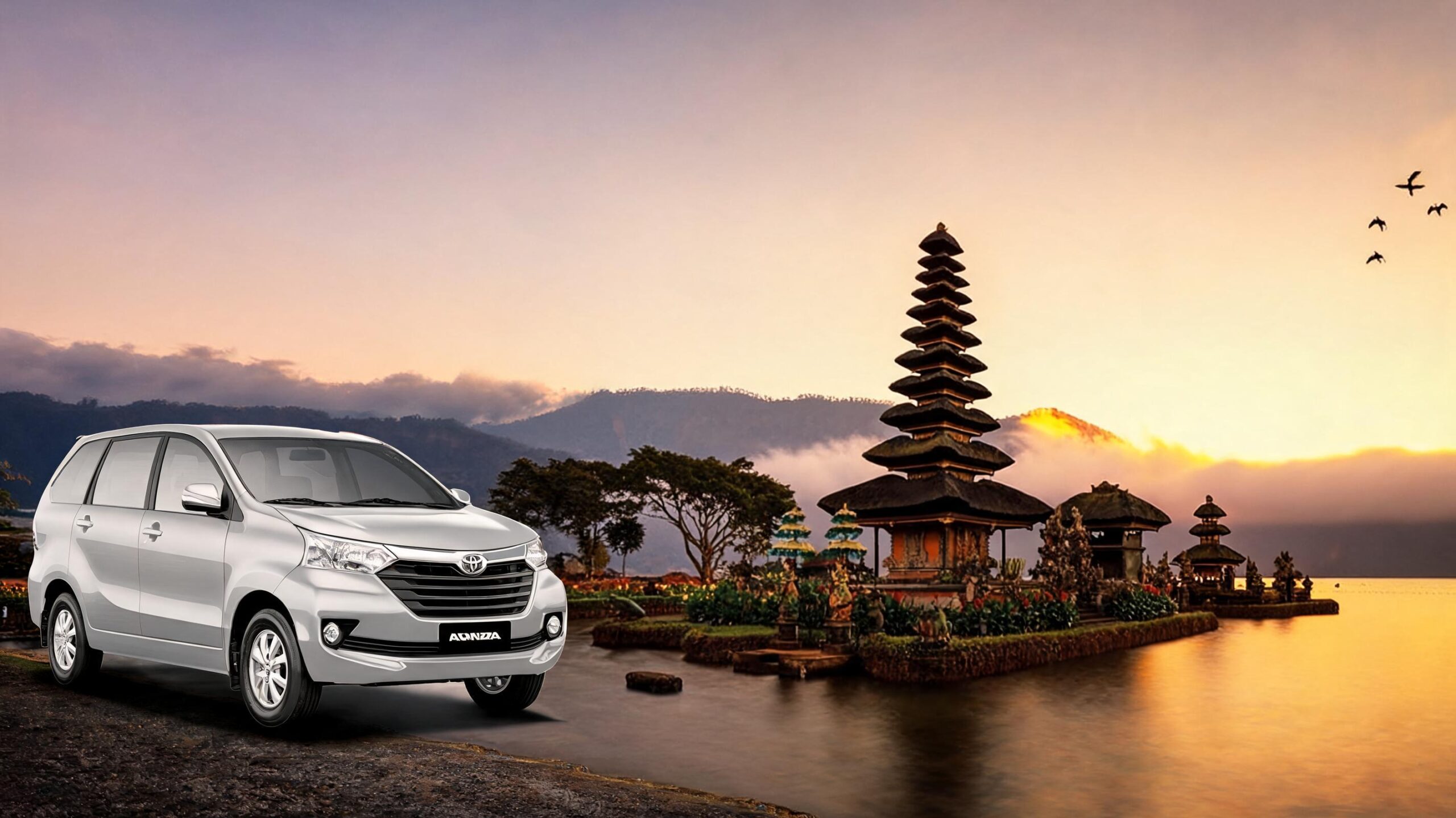 A silver car parked near a scenic Balinese temple at sunrise, with mountains and water in the background.