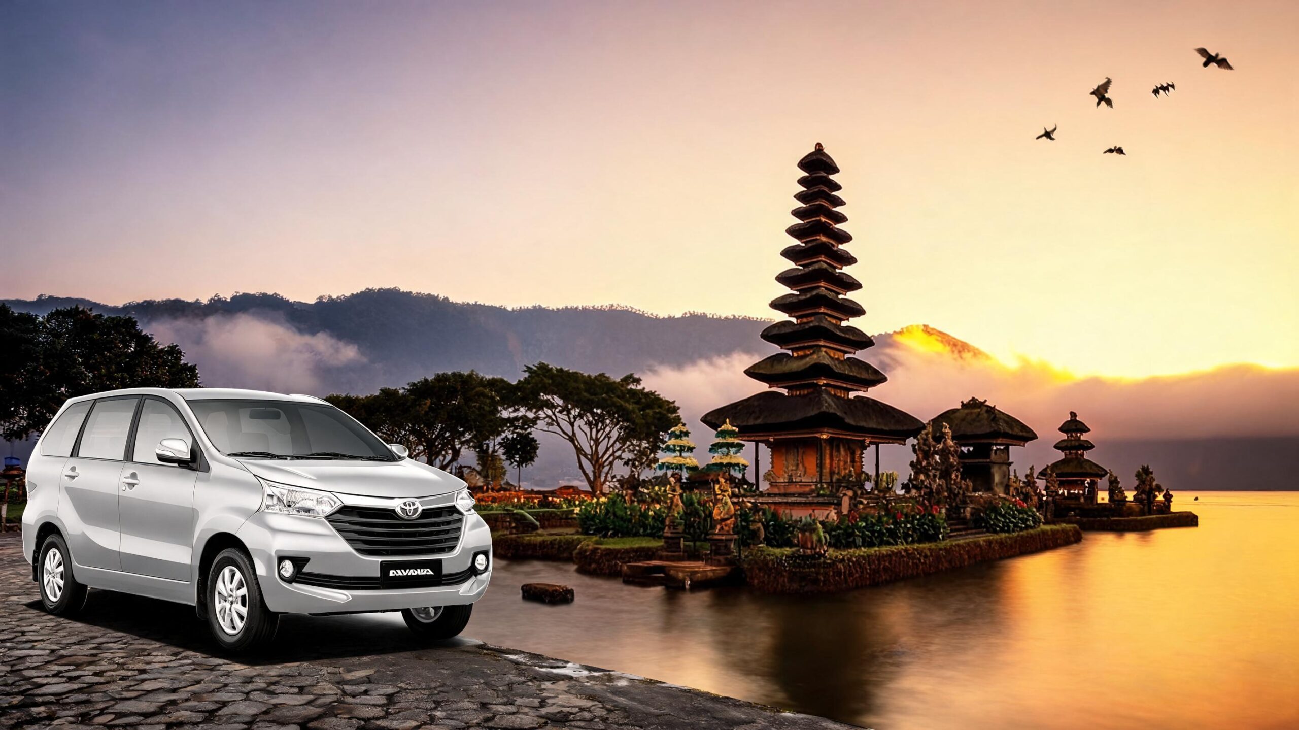 Mobil perak diparkir dekat pura Bali saat matahari terbit, dengan latar belakang pegunungan dan pepohonan.